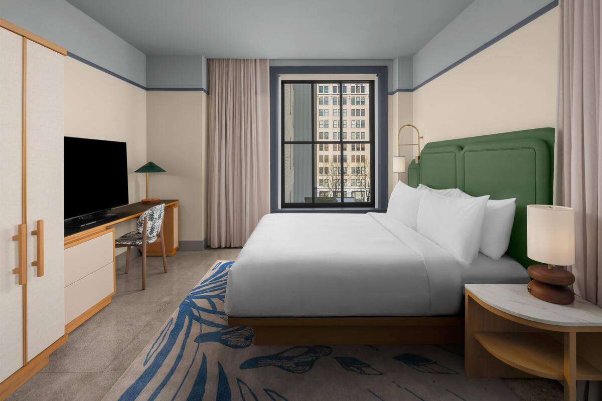 Une chambre d’hôtel équipée d’un lit, d’une télévision, d’un bureau, d’une lampe et d’une fenêtre donnant sur la ville.