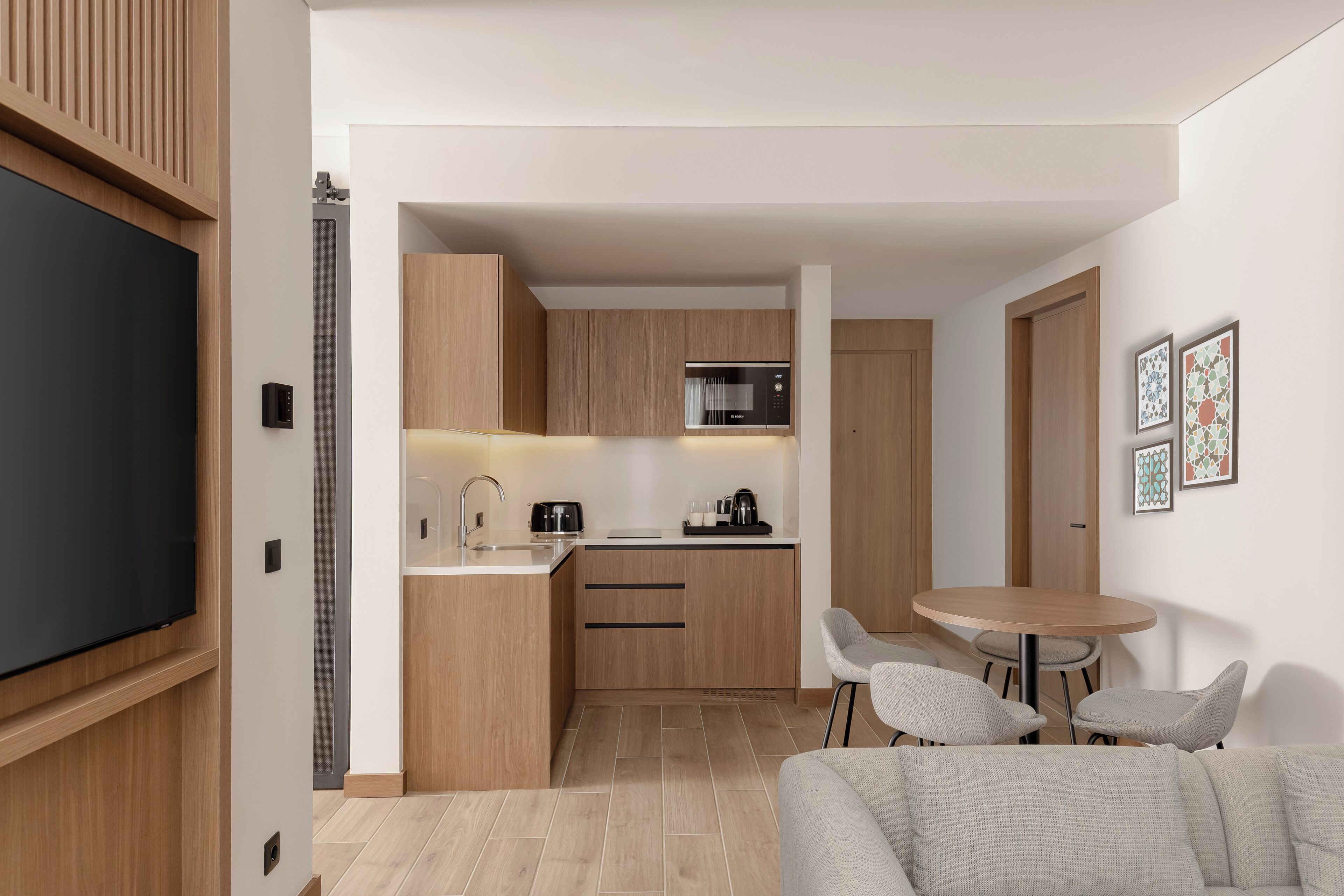 A modern kitchen with wooden cabinets, a microwave, and a coffee maker. There is a dining area with a round table and two chairs.
