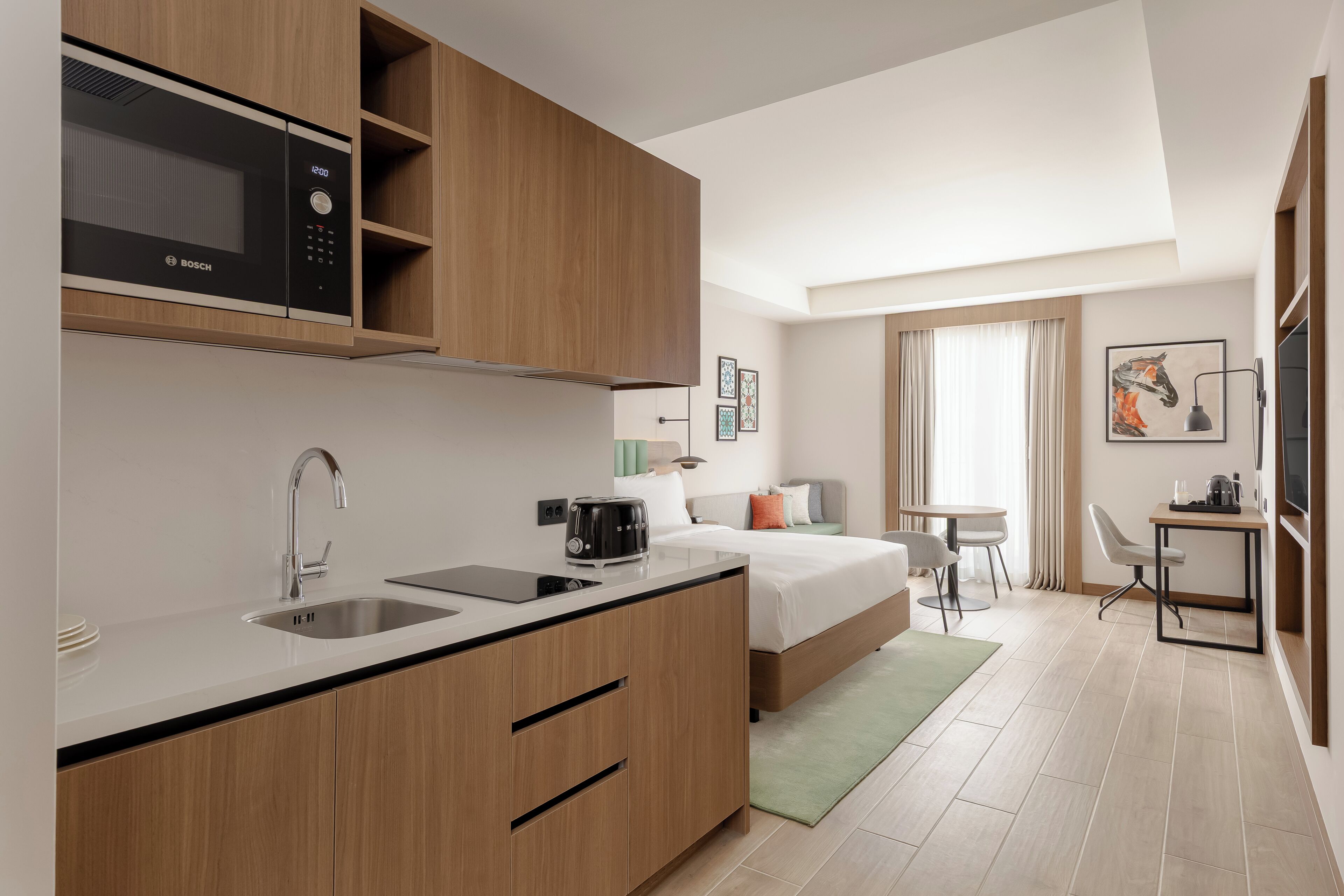 Habitación de hotel moderna con kitchenette, cama, una pequeña zona de comedor y ventana con cortinas.