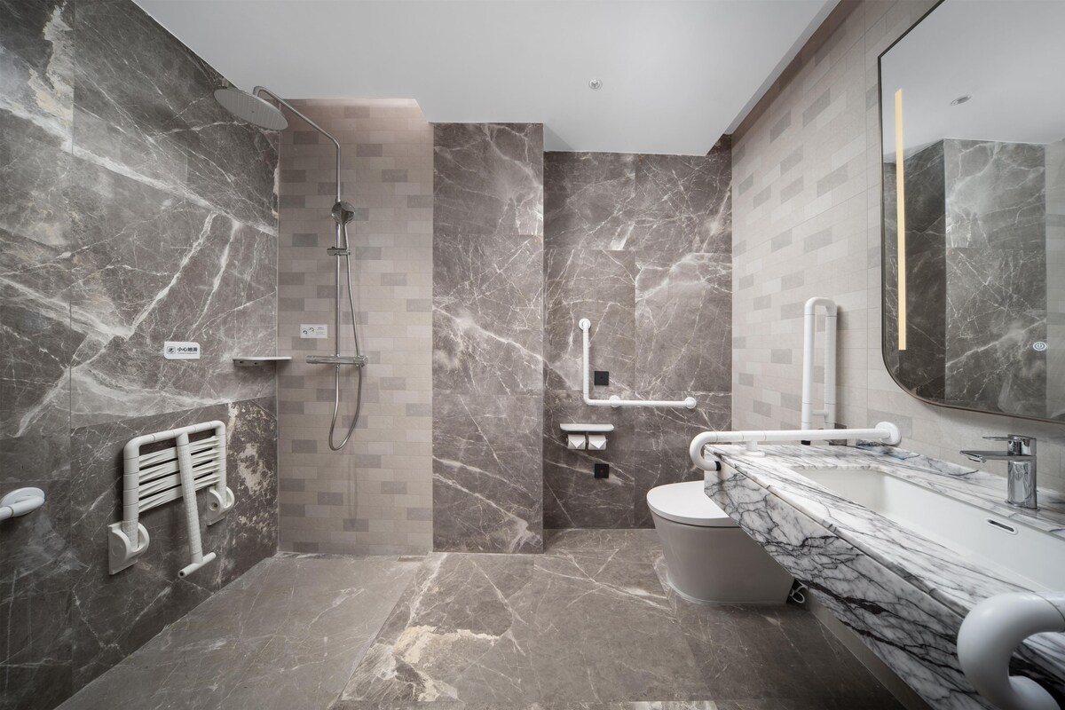 A modern bathroom with a marble shower, a toilet, and a sink with a large mirror.