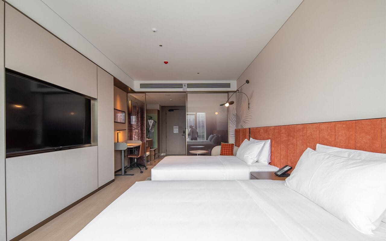 Habitación de hotel con dos camas, televisión, escritorio con silla y una mesita.