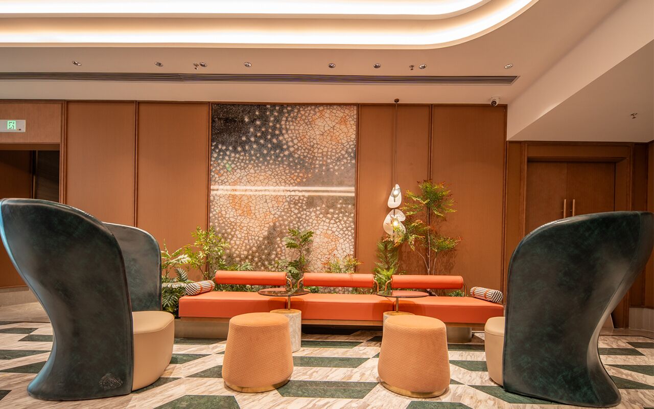 Um lobby moderno com área de estar central, parede decorativa e piso estampado.