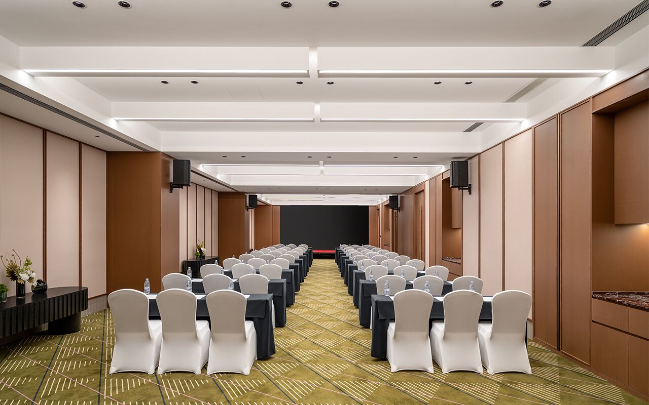 A conference room with rows of tables and chairs, a patterned carpet, and a modern ceiling design.