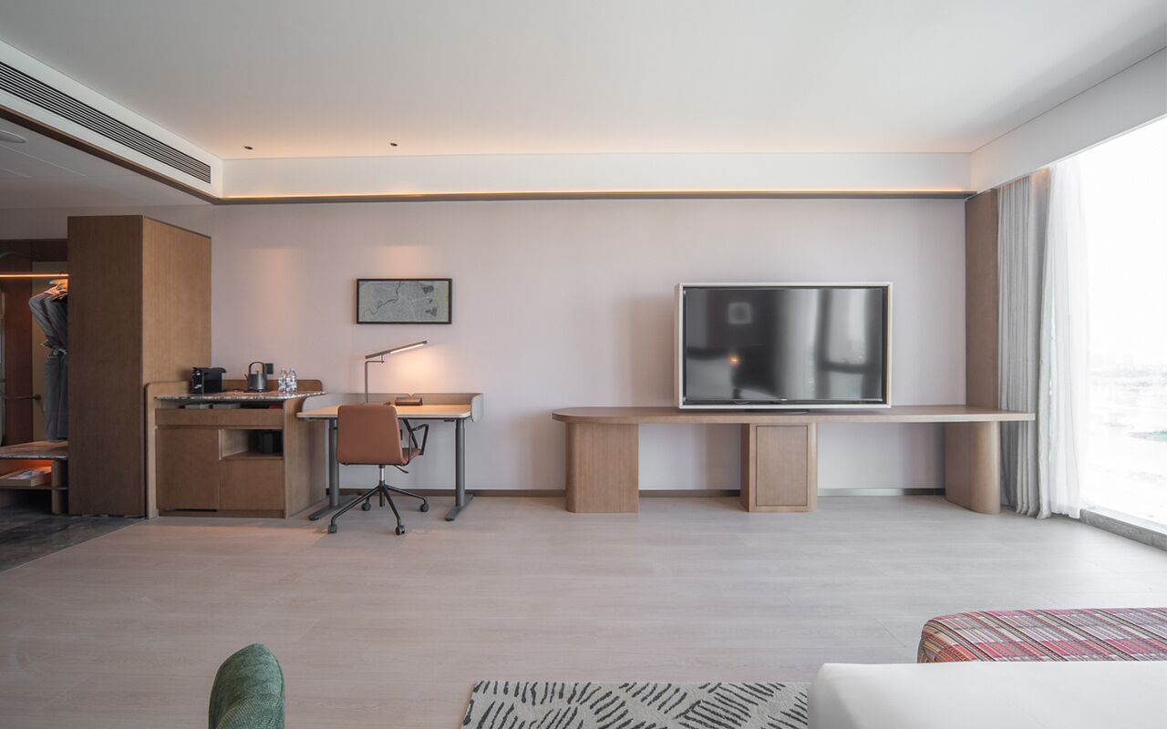 Una habitación de hotel moderna con un escritorio de madera, una televisión, un sofá y un ventanal grande.