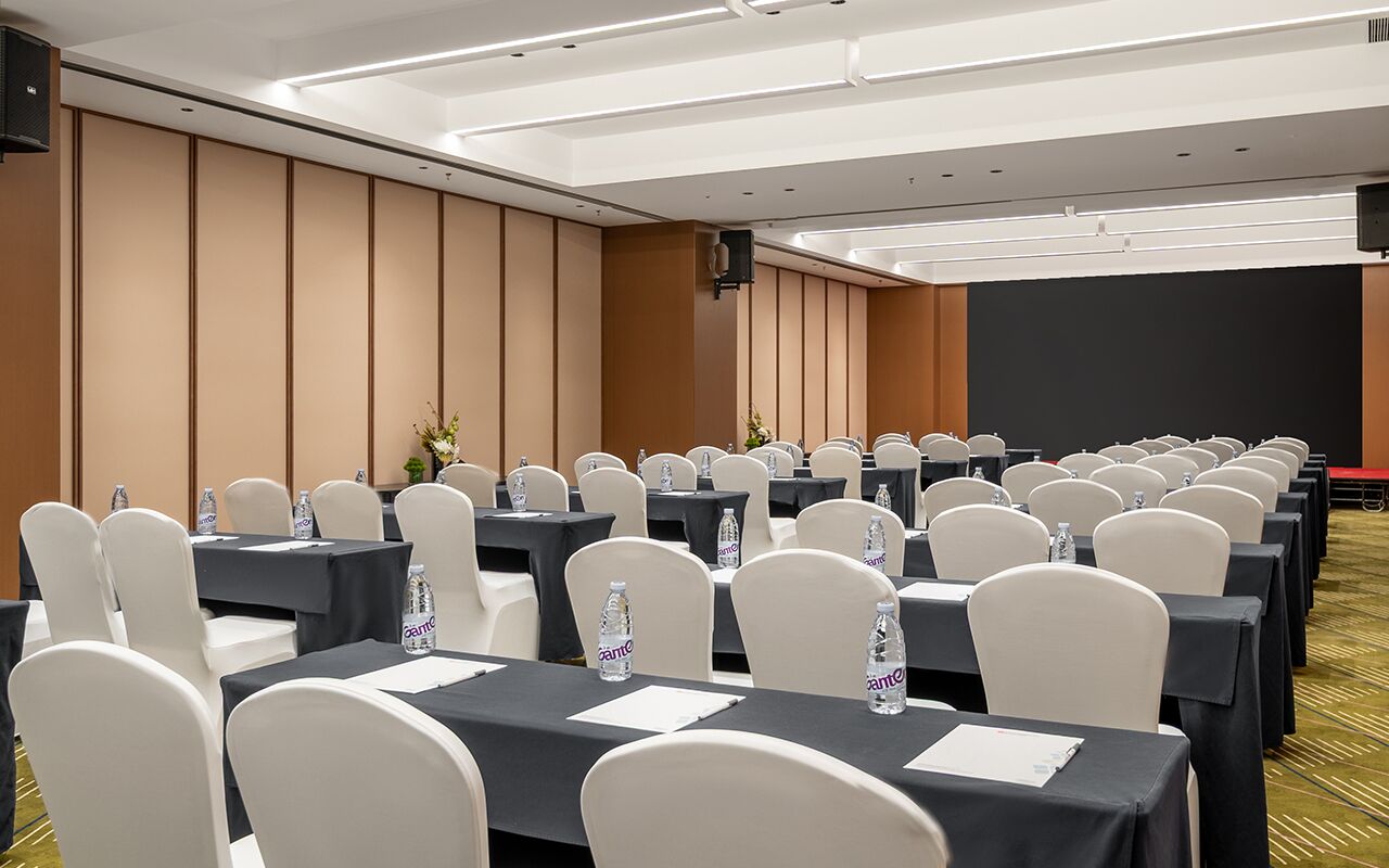 Uma sala de conferência com fileiras de mesas e cadeiras, equipada com garrafas de água e placas de identificação.