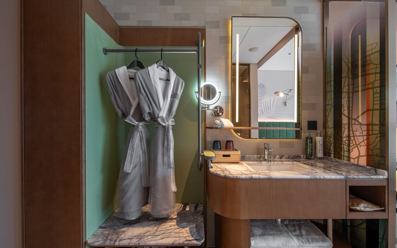 Un baño moderno con un lavamanos de mármol, un espejo y dos albornoces colgados en un perchero.