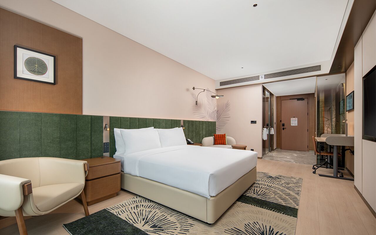 Una habitación de hotel con cama, sillón, escritorio y televisión.