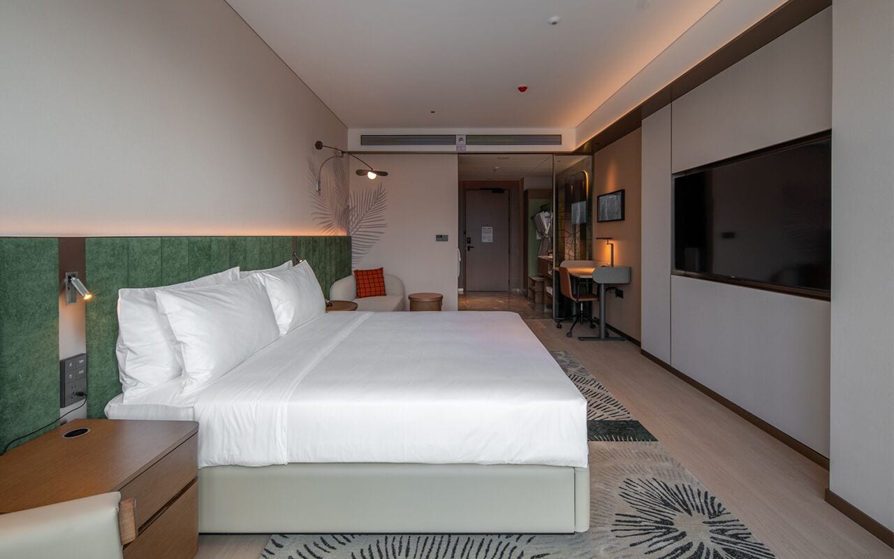 A modern hotel room with a large bed, bedside tables, a flat-screen TV, and a small desk area.