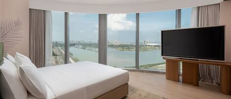 Ein modernes Hotelzimmer mit einem großen Bett, einem Flachbildfernseher und Blick auf Stadt und Fluss.