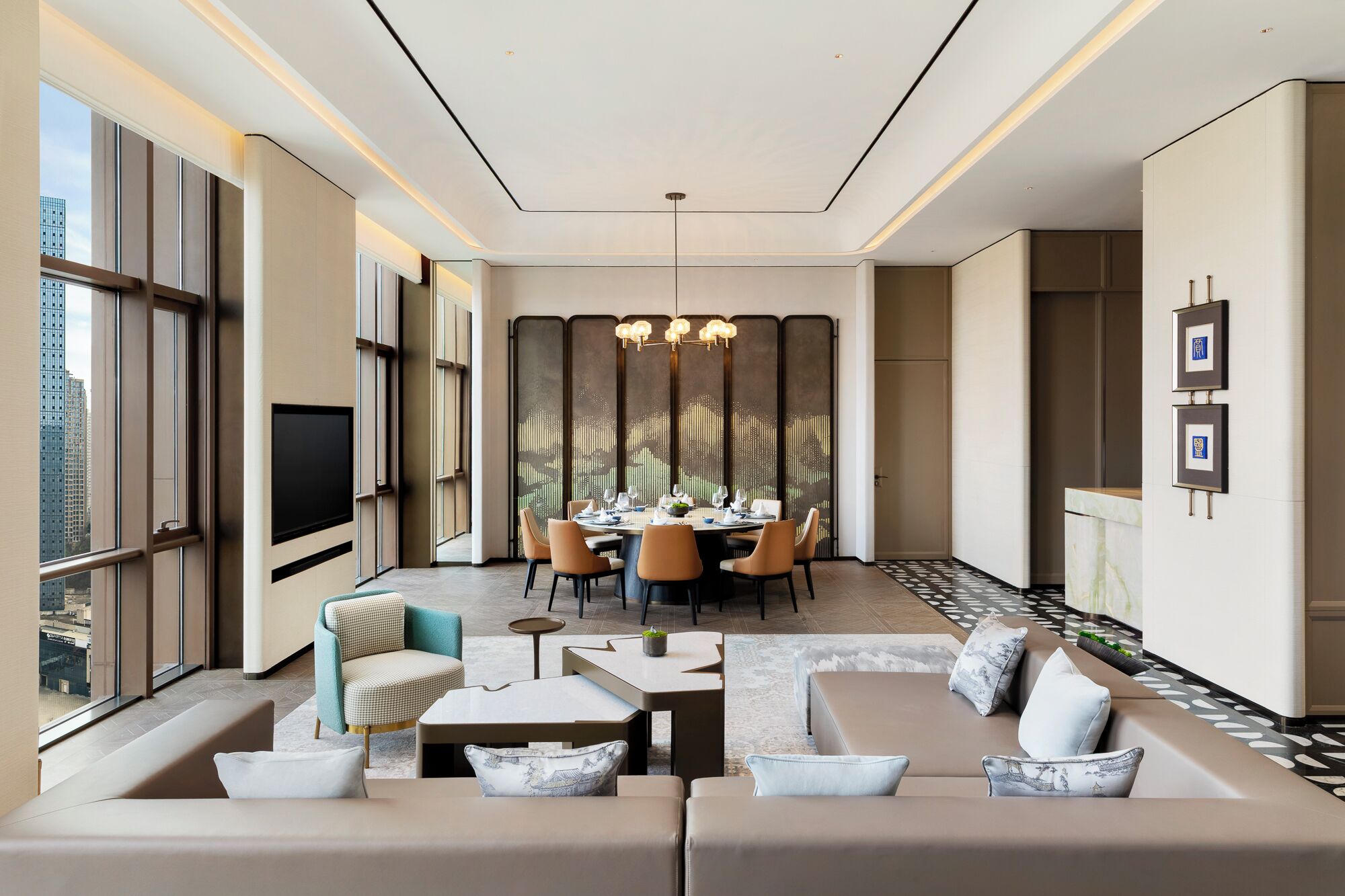 A modern hotel room with a dining area, large windows, a flat-screen TV, and a sofa set.