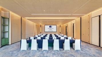 Un salón de conferencias con una larga mesa, sillas blancas y una pantalla que muestra 'DOUBLETREE by Hilton'.