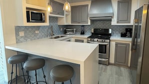 A modern kitchen with a central island, bar stools, stainless steel appliances, and pendant lighting. - La Paloma Rosarito (Playas de Rosarito)
