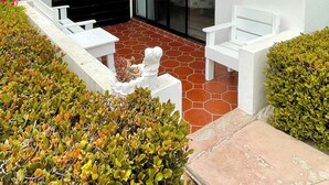 A covered patio with white furniture, a glass door, and a wall-mounted light fixture. - La Paloma Rosarito (Playas de Rosarito)
