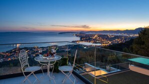 A balcony with a table and chairs overlooking a coastal cityscape at dusk. - Villa Naaria with Pool (Podstrana)