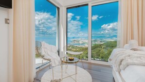 A bedroom with a large window offering a city view, a bed, a round table with a chair, and a pair of shoes on a fluffy rug. - Villa Naaria with Pool (Podstrana)