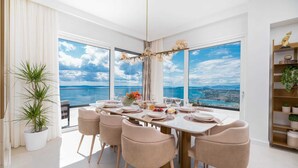 A modern dining room with a large table set for six, large windows with a city and sea view, and a decorative chandelier. - Villa Naaria with Pool (Podstrana)