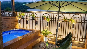 A wooden deck with a hot tub, a green umbrella, and potted plants.
