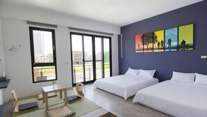 A modern hotel room with two beds, a small table, a chair, and large windows offering a view of the city.