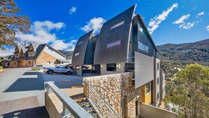 A modern house with a stone facade, a carport, and a view of a hilly landscape.