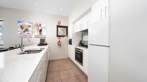 A modern kitchen with white cabinets, a stainless steel sink, and a built-in oven. There are two posters on the wall and a fire extinguisher mounted on the wall.