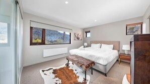 A modern bedroom with a large bed, a bench, a view of mountains through the windows, and a cowhide rug.