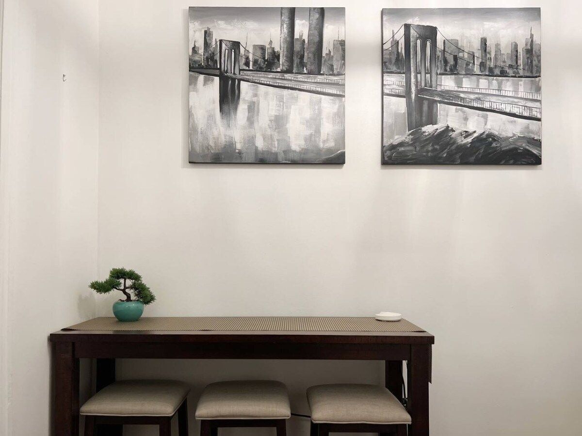 A room with a wooden table, two chairs, and two wall-mounted paintings of a bridge.
