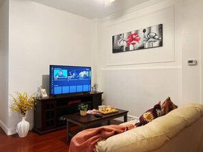 A living room with a flat-screen TV, a sofa, a coffee table, and a wall-mounted artwork.