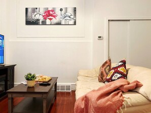 A living room with a sofa, a coffee table with a plant and snacks, a painting on the wall, and a television.