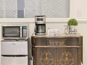 A kitchenette with a microwave, coffee maker, and a small potted plant on a cabinet.
