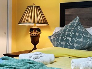 A hotel room with a bed, a bedside lamp, a pillow, and a blanket.