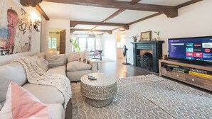 A living room with a sofa, ottoman, and a TV on a wooden stand. - Luxury Villa w/ Pool, Mountain Views near NASA (Altadena)