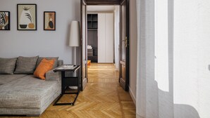 Una sala de estar moderna con un sofá gris, una mesita y una lámpara. Se ve un pasillo que conduce a un armario y una puerta.