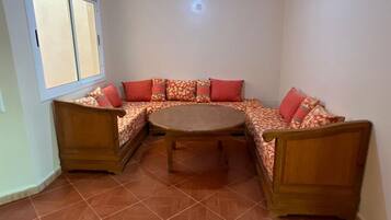 Habitación de esquina con un banco de madera y una mesa redonda, una ventana y una lámpara fijada a la pared.