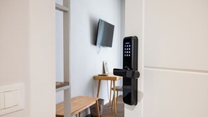 Una habitación moderna con televisor de pared, un banco de madera y una puerta con cerradura digital.