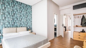 Un dormitorio moderno con una cama grande, suelo de madera, una pared con diseño geométrico y un vestidor con espacio para colgar ropa.