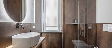 A modern bathroom with a large mirror, a wooden vanity, a shower enclosure, and a toilet.