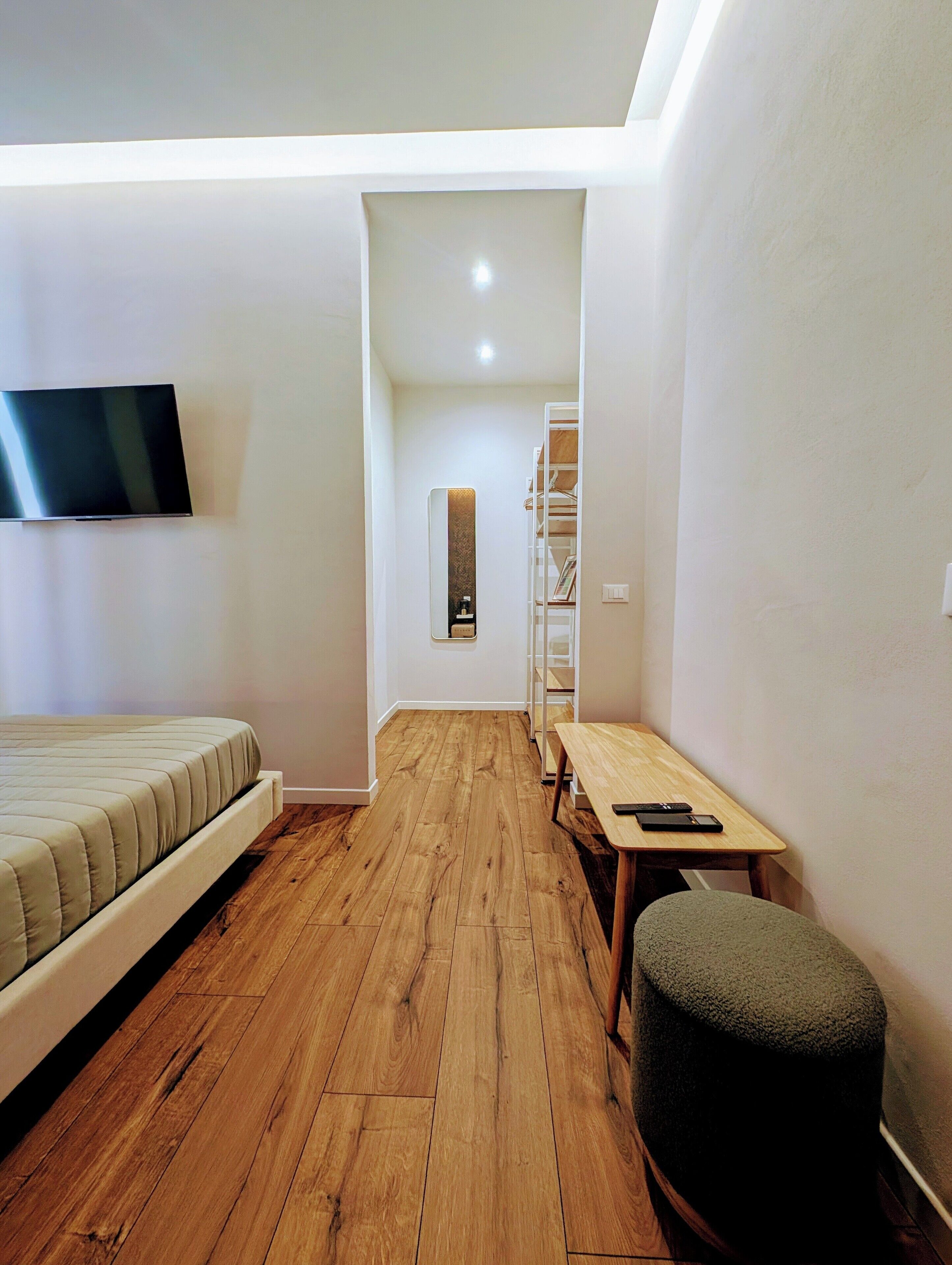 A modern, compact room with a bed, a desk, and a TV mounted on the wall.