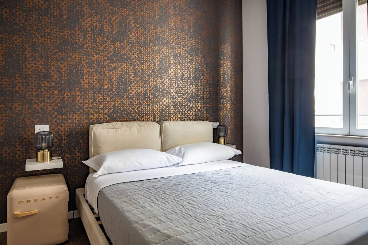 Una habitación de hotel con cama, mesita de noche, lámpara y radiador.