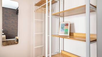 A room with a wooden floor, a white wall, and a mirror. There are shelves with a welcome sign and a small table.