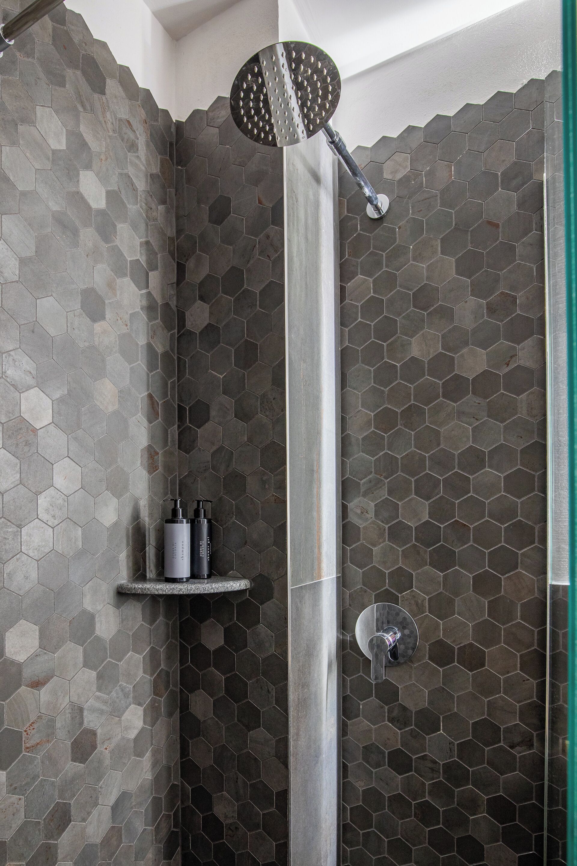 A shower with a hexagonal tile pattern, a handheld showerhead, and a shelf with toiletries.