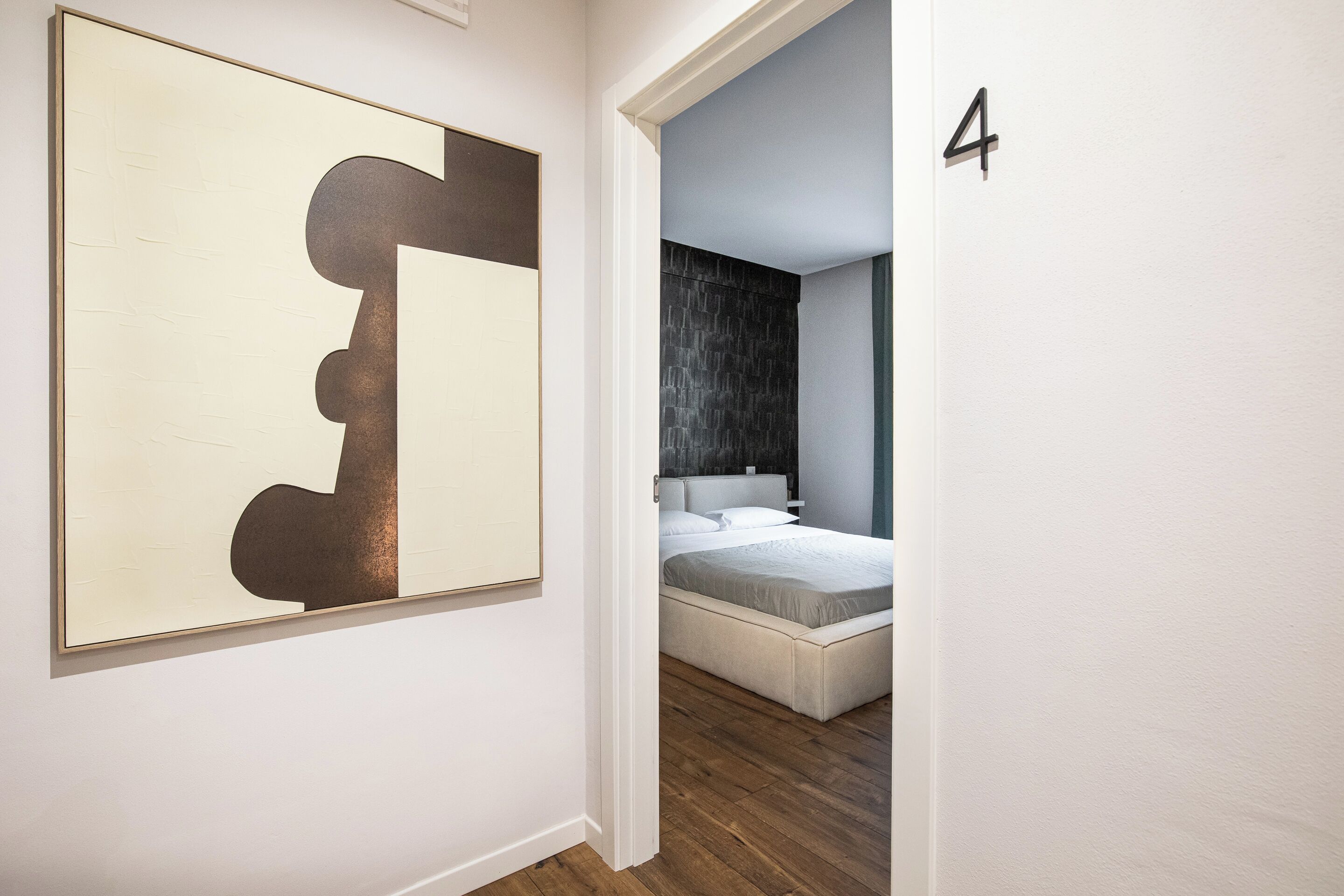 Un dormitorio moderno con un cuadro abstracto grande en la pared, una cama bien tendida y una pared oscura con textura detrás de la cama.