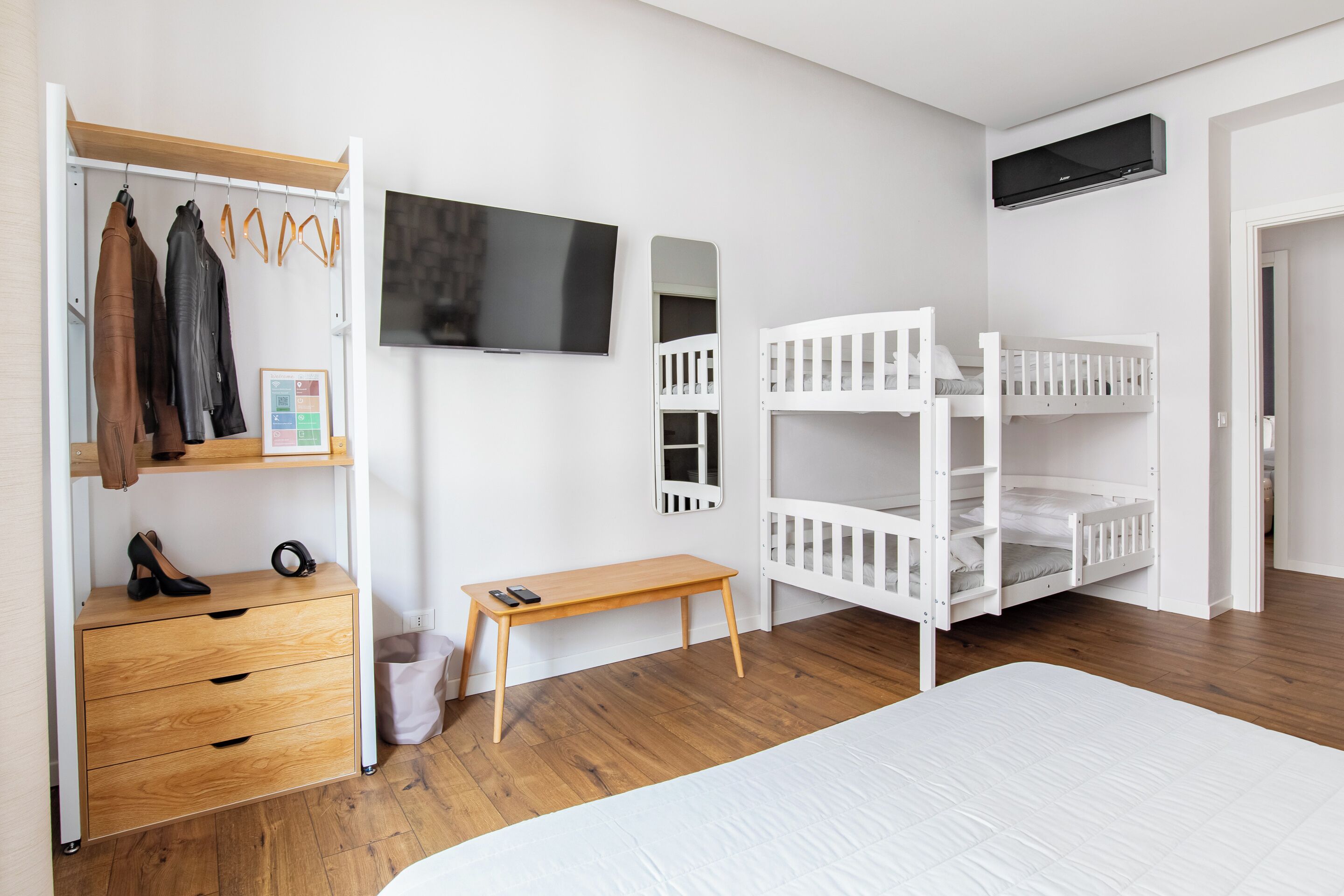 A bedroom with a bunk bed, a wooden dresser, a TV, and a coat rack.