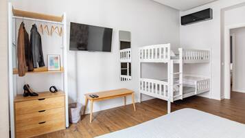 A bedroom with a bunk bed, a wooden dresser, a TV, and a coat rack.