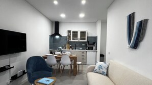 A modern living room with a sofa, a blue armchair, a small table, and a TV mounted on the wall.