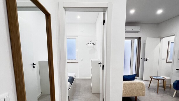 A modern, well-lit room with a large mirror, a bed, a seating area with a small table, and a wardrobe.