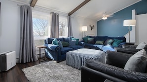 A modern living room with a blue sofa set, a black leather chair, a patterned ottoman, a standing lamp, and a ceiling fan. - Mountain side, remodeled  4 br neat trail head. (Wilmington)