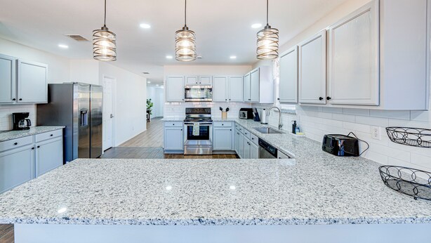 A modern kitchen with granite countertops, stainless steel appliances, white cabinetry, and pendant lighting. - Tremendous space with covered patio in central McKinney (McKinney)
