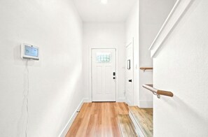 Un pasillo con una puerta blanca, un termostato en la pared y un banco de madera.