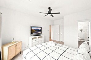 Habitación de hotel con cama, televisor sobre un mueble bajo, armario y ventilador de techo.