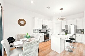 Una cocina moderna con armarios blancos, una isla central y taburetes de bar.